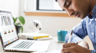 A Person in front of laptop writing on paper.
